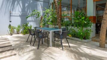 A patio with a table and chairs, surrounded by potted plants and a palm tree.