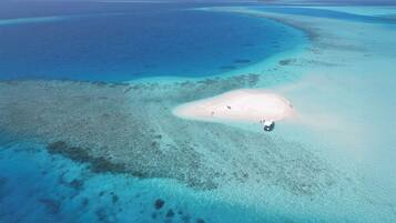 Vista aérea de una playa con aguas turquesas cristalinas, una isla arenosa y un pequeño bote.