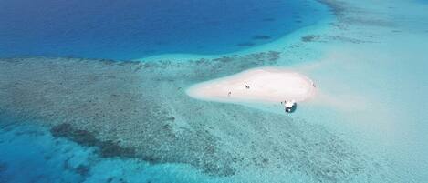 Vista aerea di una spiaggia con acque turchesi cristalline, un'isola sabbiosa e una piccola barca.