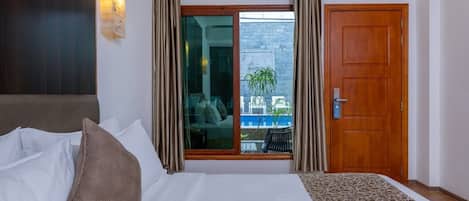 Habitación de hotel con cama, ventana con cortinas, puerta de madera y vista al exterior.