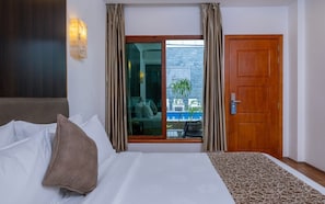 A hotel room with a bed, a window with curtains, a wooden door, and a view of the outside. - Kaani Village & Spa (Maafushi)