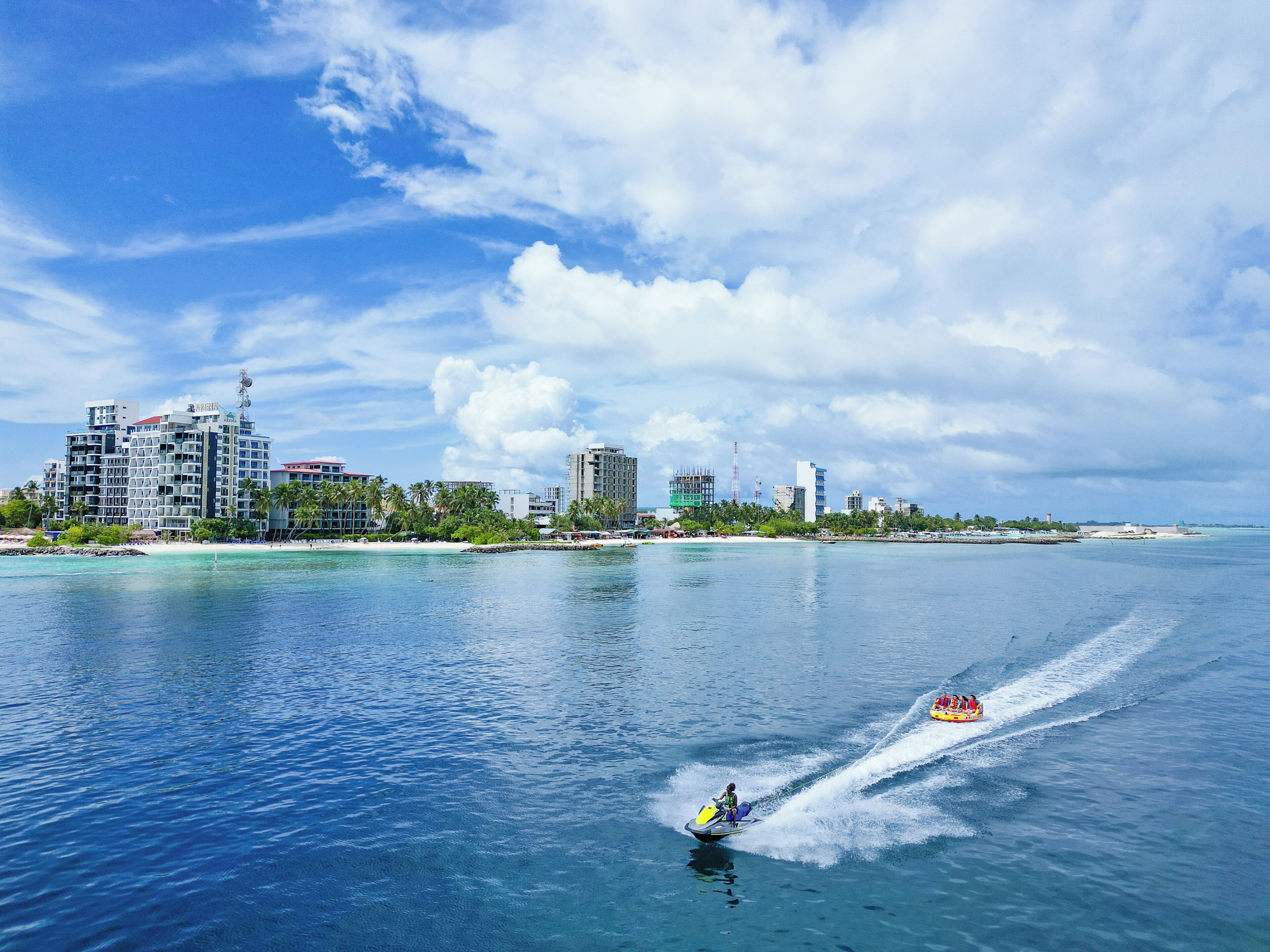 A coastal cityscape with a clear sky, a body of water, and a jet ski in motion.