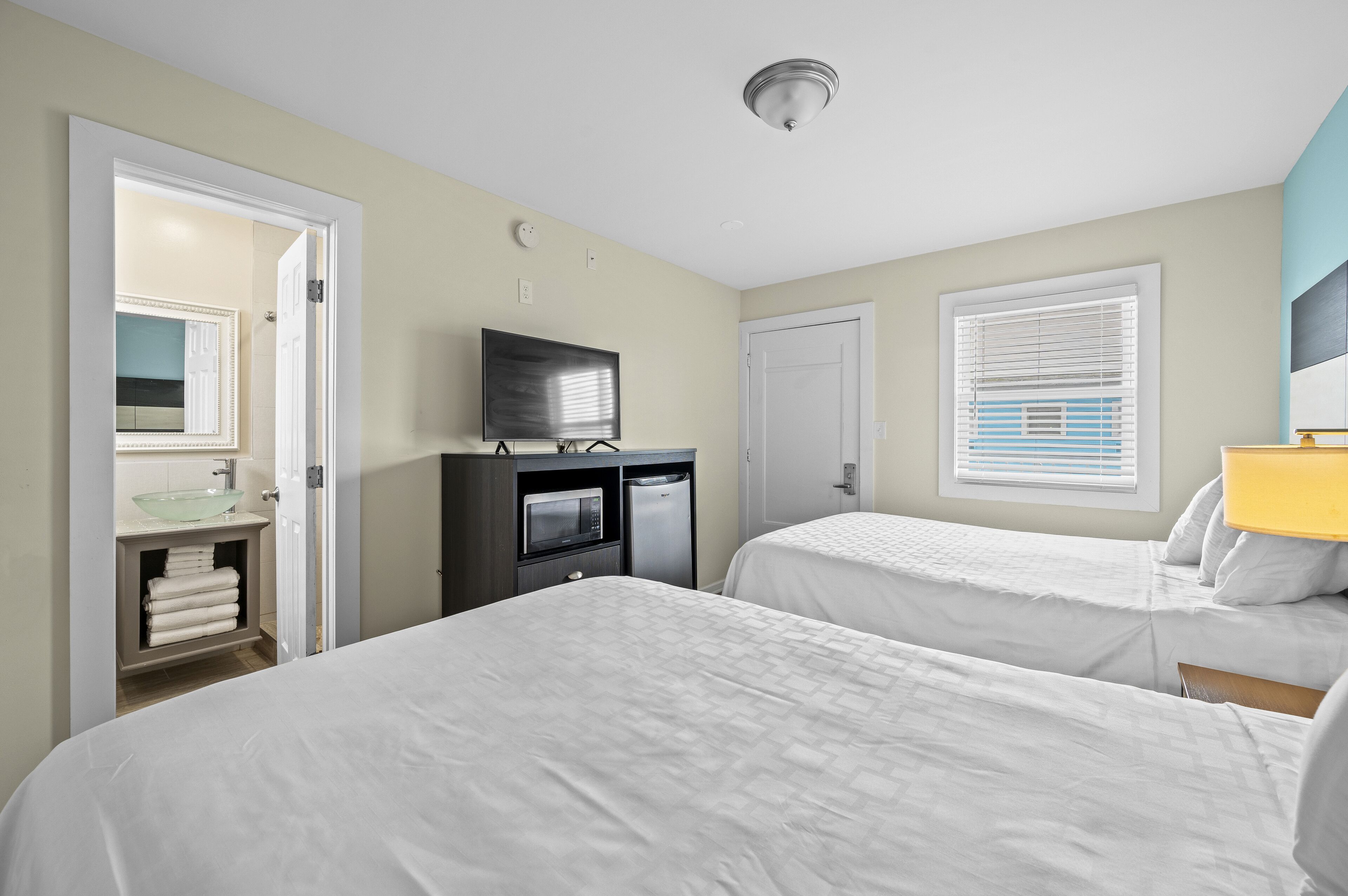 Habitación de hotel con dos camas, televisión, microondas y baño con lavamanos y espejo.