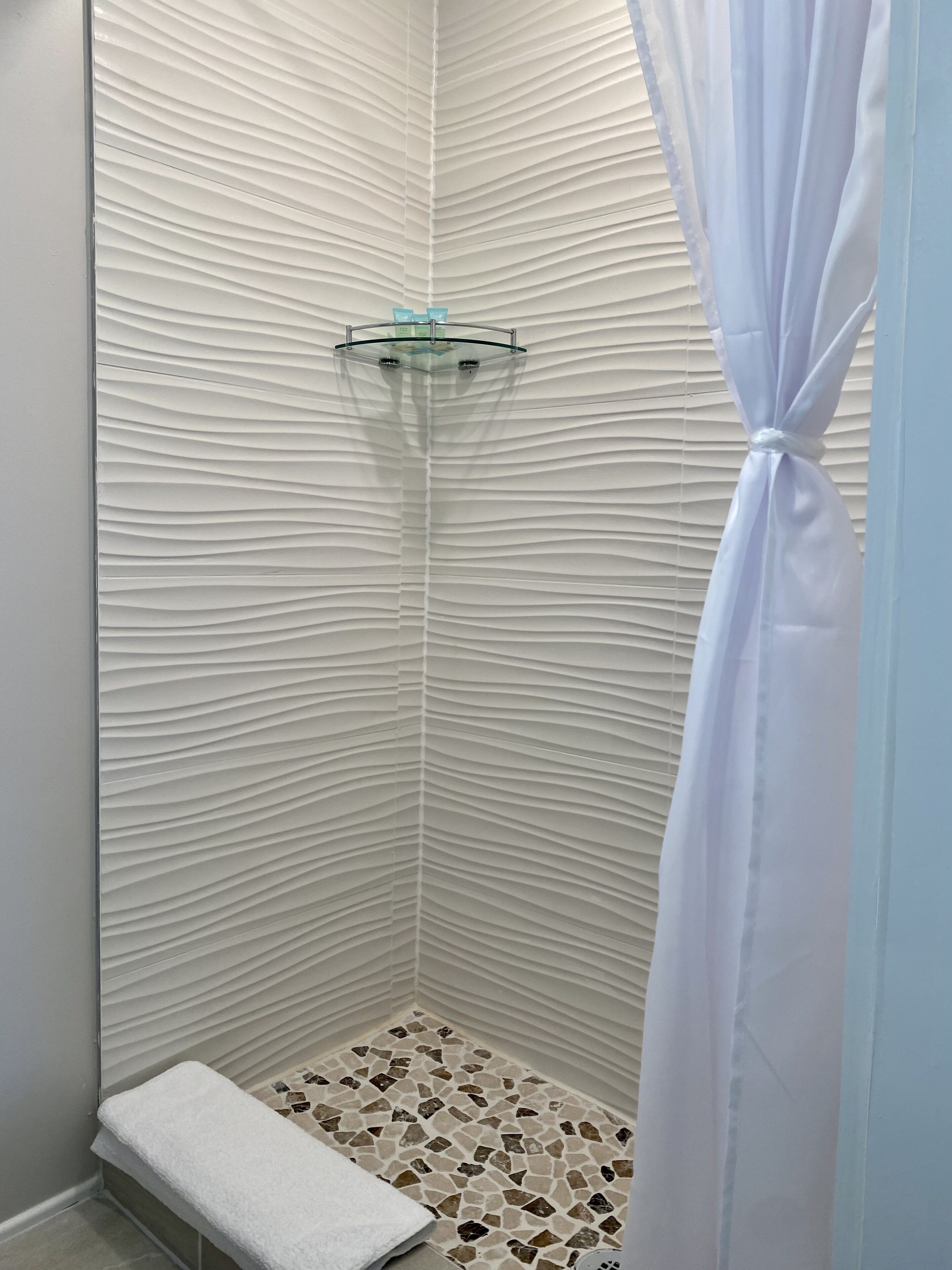 A shower with a textured wall, a glass shelf, a tiled floor, and a white towel.
