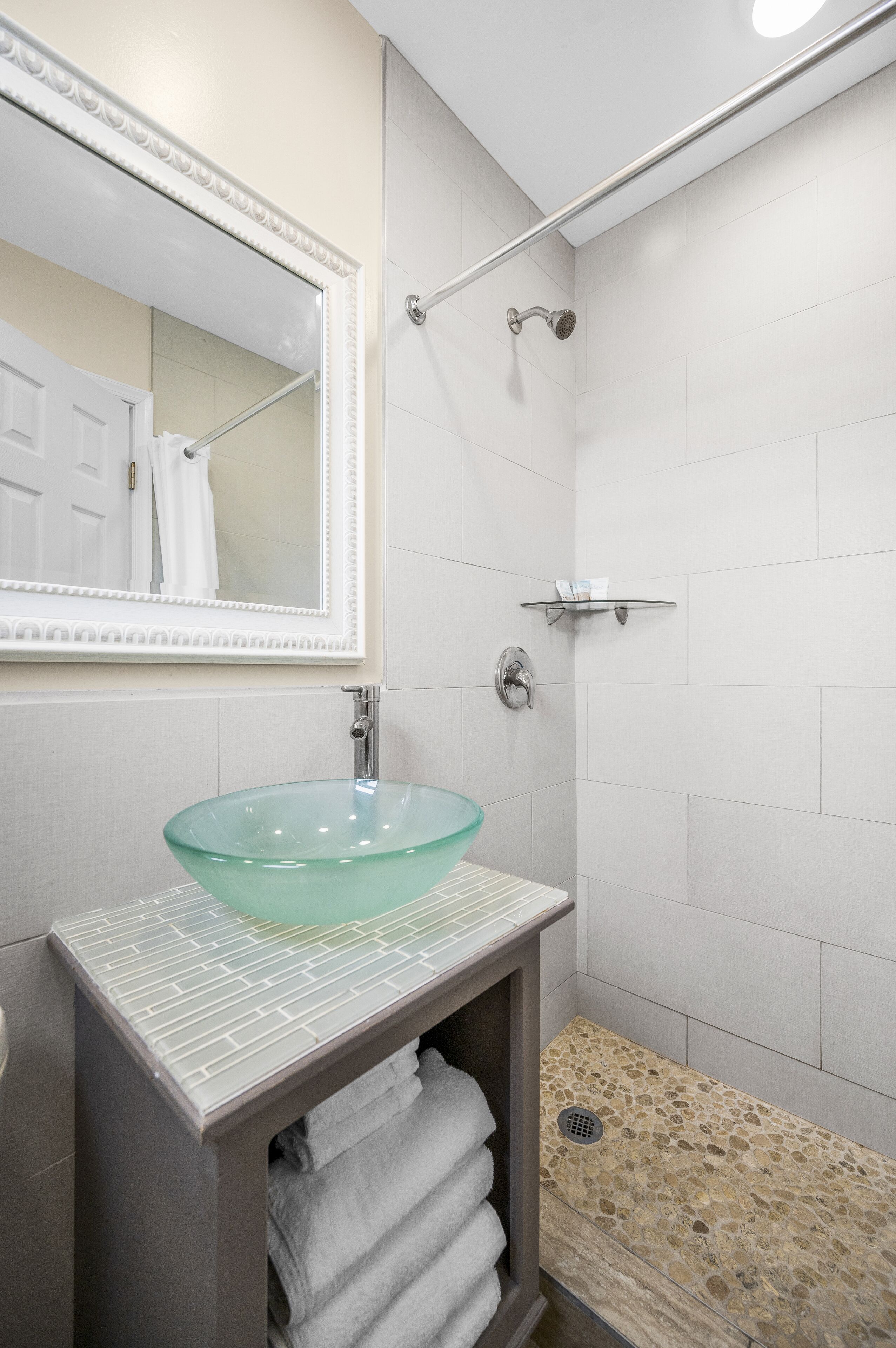 A bathroom with a glass sink, a mirror, a shower, and a towel rack.