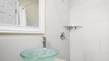 A bathroom with a glass sink, a mirror, a shower, and a towel rack.