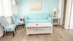 Una sala de estar con un sofá azul claro, dos sillones a rayas, una mesa de centro blanca y una lámpara sobre una mesita.