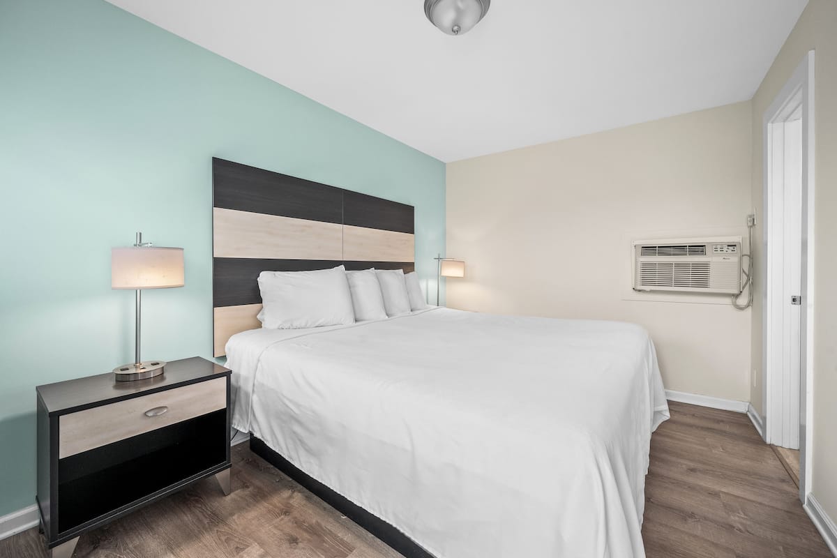 A bedroom with a bed, nightstand, lamp, and air conditioning unit.
