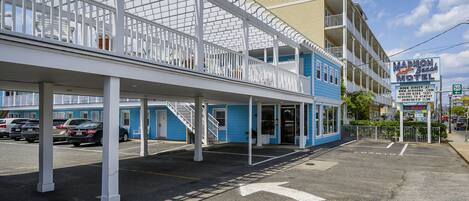 Ein Motel mit überdachtem Parkplatz, ein zweistöckiges Gebäude mit Balkonen und einem Schild, das den Namen und die Annehmlichkeiten des Motels bewirbt.