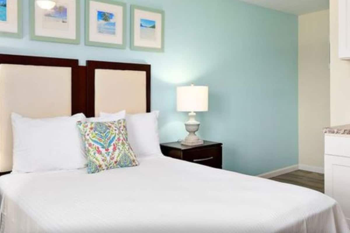 A hotel room with a bed, a nightstand, a lamp, and a wall with framed pictures.