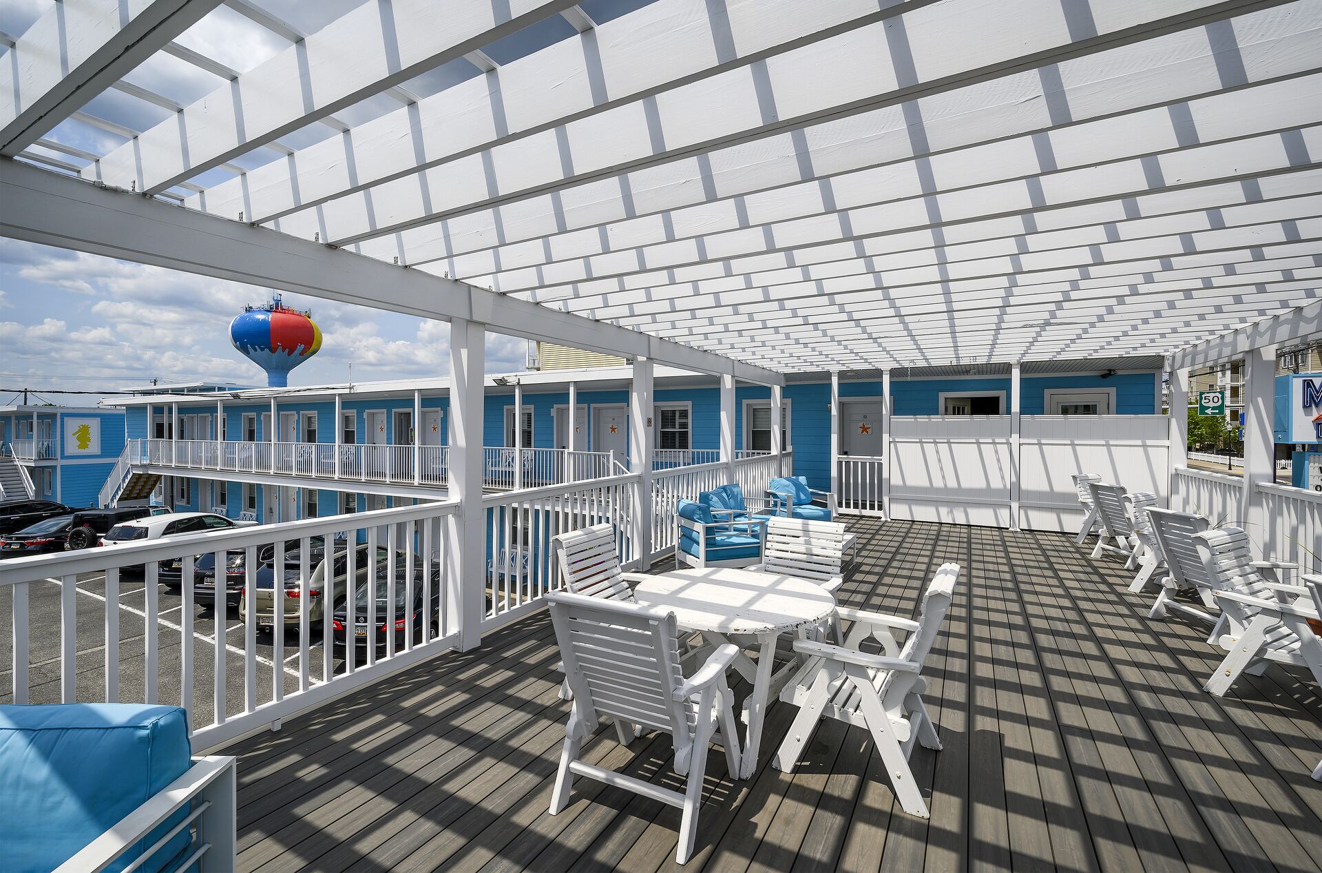 A covered outdoor deck with white railings, blue and white buildings in the background, and a red and yellow water feature.