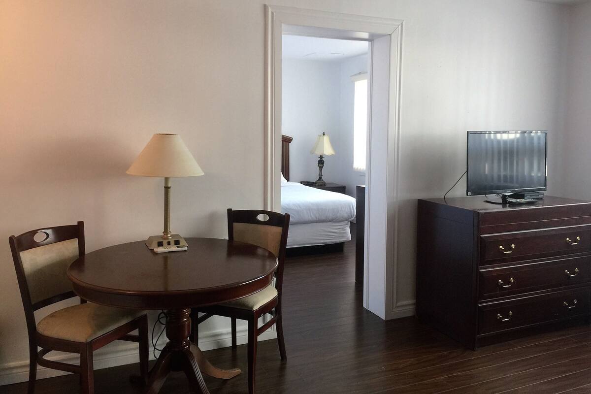 A hotel room with a dining table, chairs, a TV on a dresser, and a bed in the background.