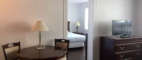 A hotel room with a dining table, chairs, a TV on a dresser, and a bed in the background.