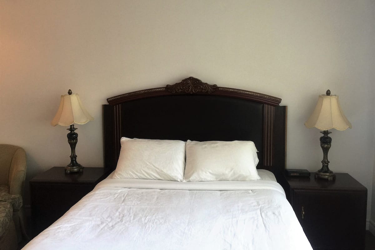 A neatly made bed with white linens, a dark wooden headboard, and two bedside lamps on matching nightstands.