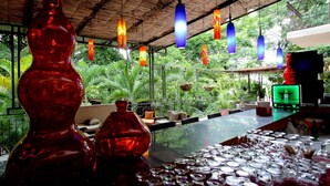 A bar area with a glass table, red decorative vases, hanging pendant lights, and a view of lush greenery outside. - La Reserve Hotel (Petionville)