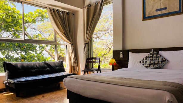 A hotel room with a bed, a sofa, a chair, and a window with curtains. - La Reserve Hotel (Petionville)