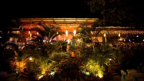 An outdoor restaurant area with a covered seating area, surrounded by lush greenery and decorative lighting. - La Reserve Hotel (Petionville)