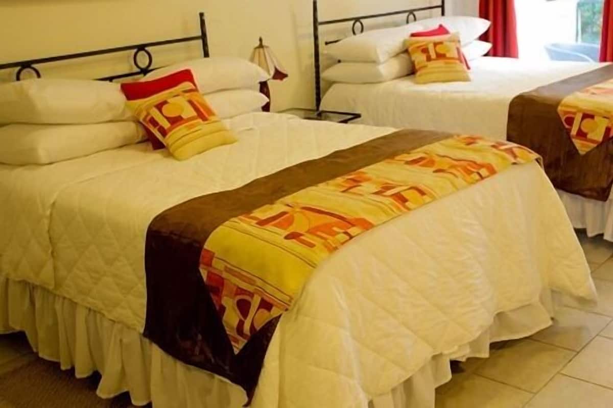Ein Hotelzimmer mit zwei Betten, jeweils mit weißer Bettwäsche und einer gemusterten Decke.