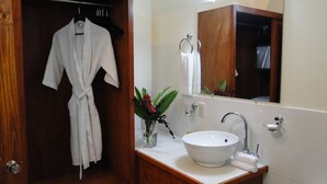 A bathroom with a white sink, a mirror, and a robe hanging on a rack. - La Reserve Hotel (Petionville)