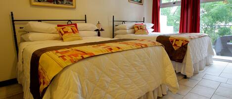 A hotel room with two beds, a large window with red curtains, and artwork on the walls.