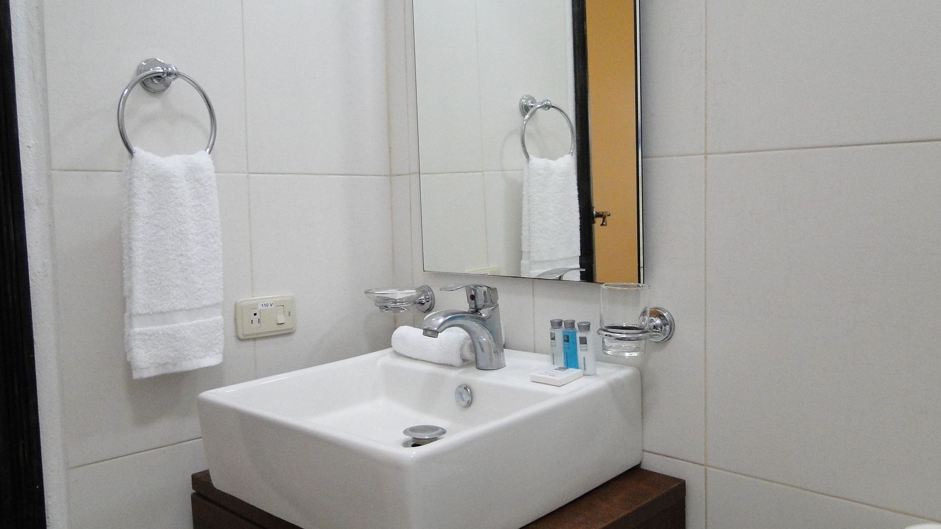 Un baño con un lavabo blanco, un espejo y dos anillas para toallas.