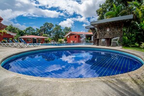 Relax by the serene pool surrounded by lush greenery and a clear sky, with lounge chairs and a water spout nearby.