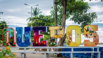 Welcome to the vibrant outdoor space with a tropical theme, featuring a colorful 'QUEPOS' sign amidst lush surroundings.
