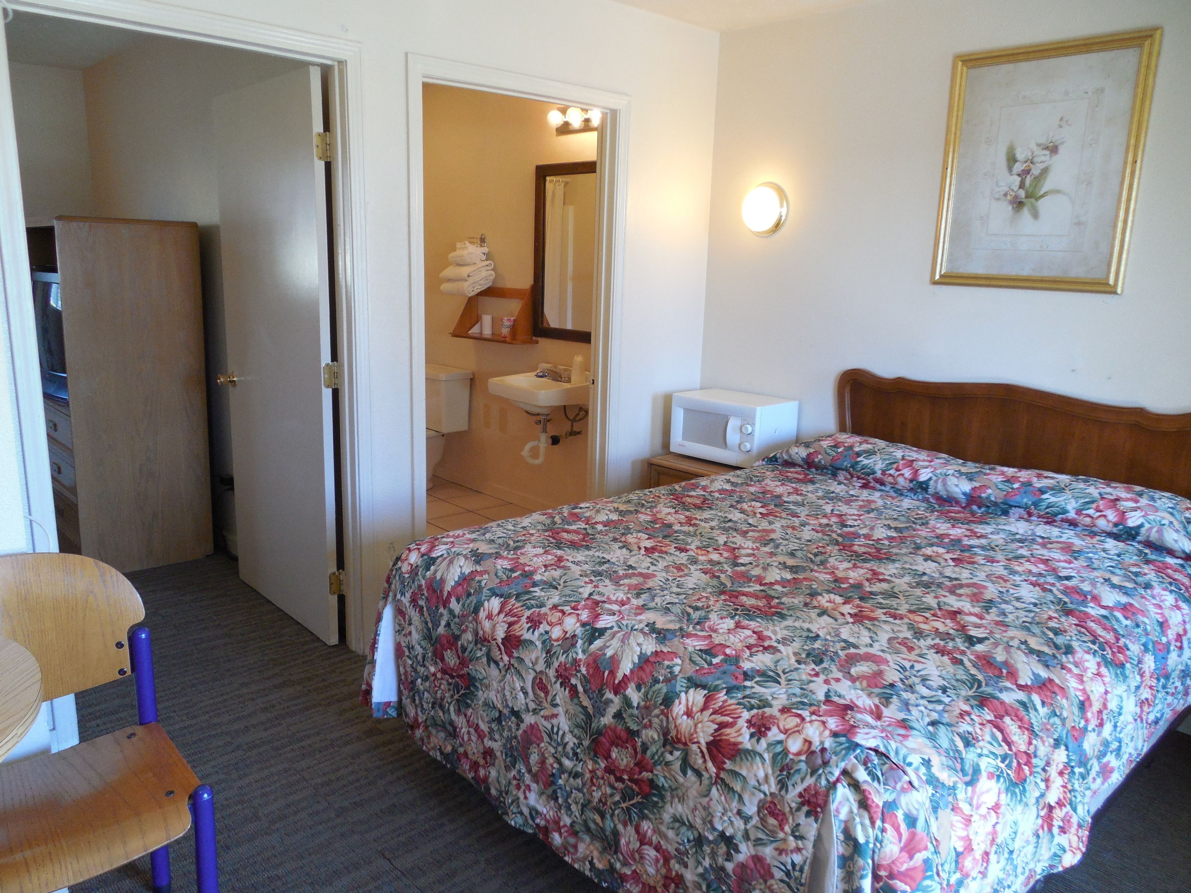 A hotel room with a bed, a chair, a microwave, a sink, and a door leading to a bathroom.