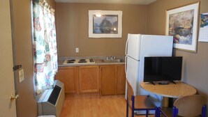 A compact kitchen with wooden cabinets, a stove, a refrigerator, and a small dining table with two chairs.