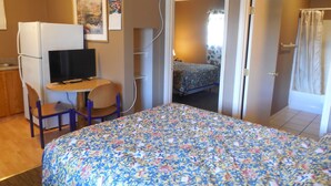 A bedroom with a bed, a desk with a chair, a television, and a door leading to a bathroom.