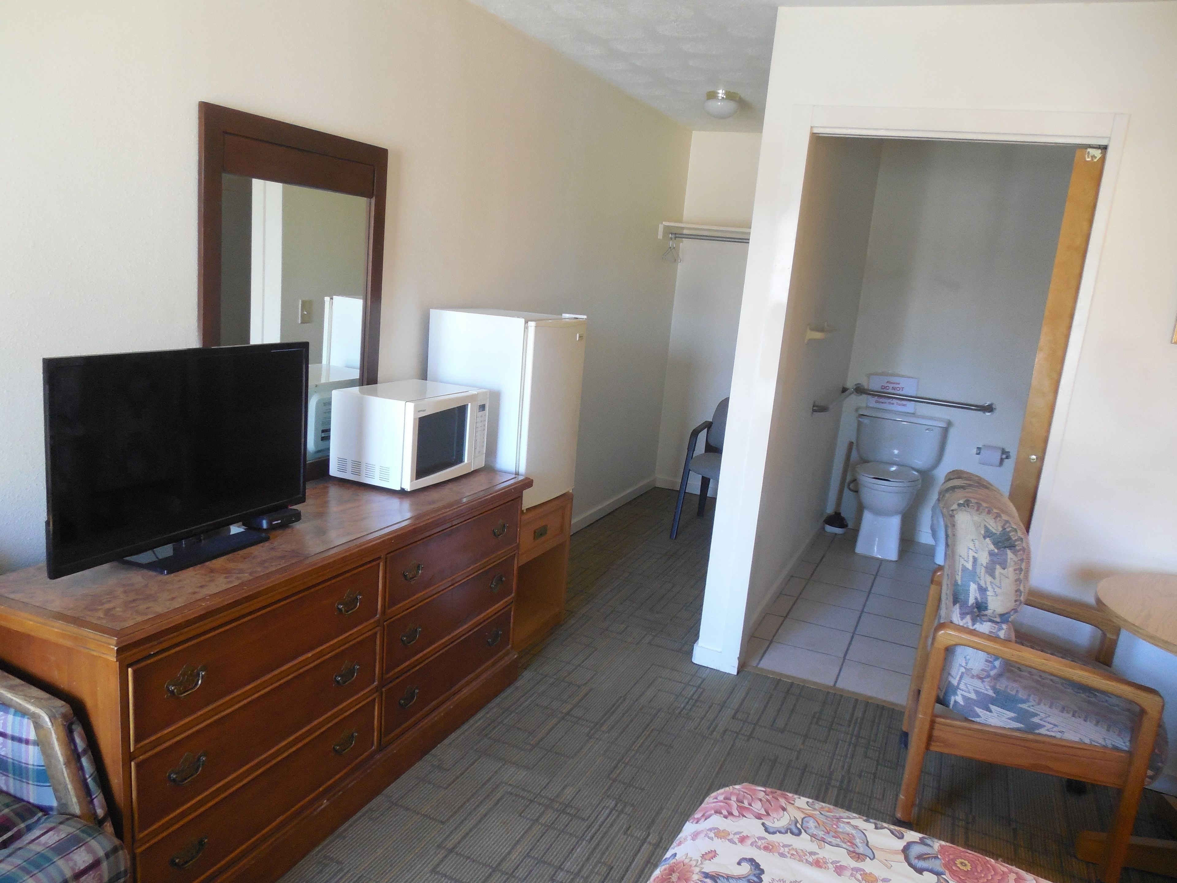 A hotel room with a wooden dresser, a television, a microwave, a chair, and a small table.