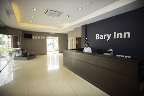 A reception area with a dark reception desk, a receptionist, and a sign that reads "Bary Inn." - Bary Inn KLIA Transit Hotel (Sepang)