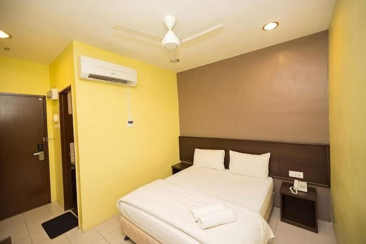 A hotel room with a bed, a nightstand, a wall-mounted air conditioner, a ceiling fan, and a door.