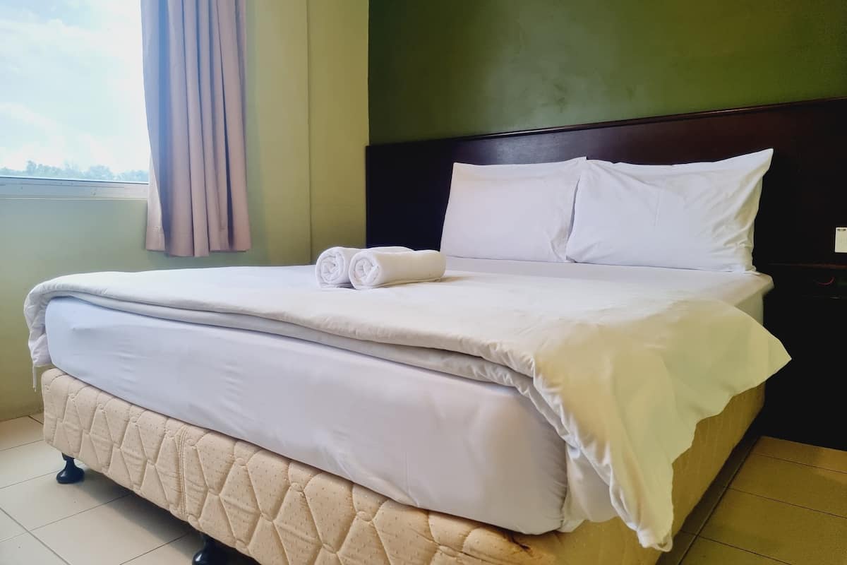 A neatly made bed with white linens and a quilted cover, a dark headboard, and a view of the sky through a window with curtains.