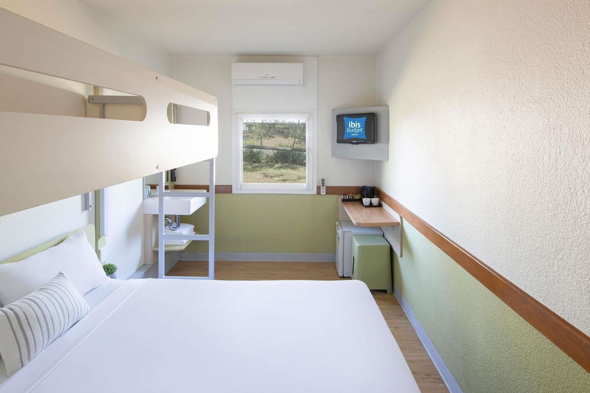 Habitación de hotel con literas, una kitchenette pequeña, televisión y ventana con vistas al exterior.
