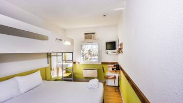 A compact hotel room with a bunk bed, a desk with a chair, a window with a view, and a television.