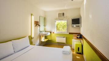 Habitación de hotel con cama, ventana, lavamanos, espejo, calefacción y televisión.