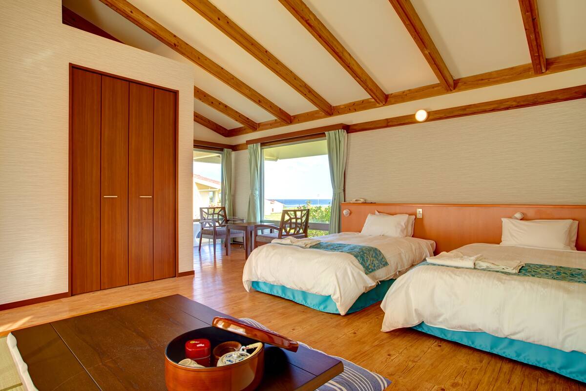 Ett hotellrum med två sängar, trägolv, en matplats med bord och stolar samt utsikt över omgivningarna.