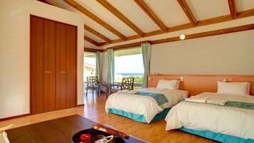 A hotel room with two beds, wooden flooring, a dining area with a table and chairs, and a view of the outdoors.