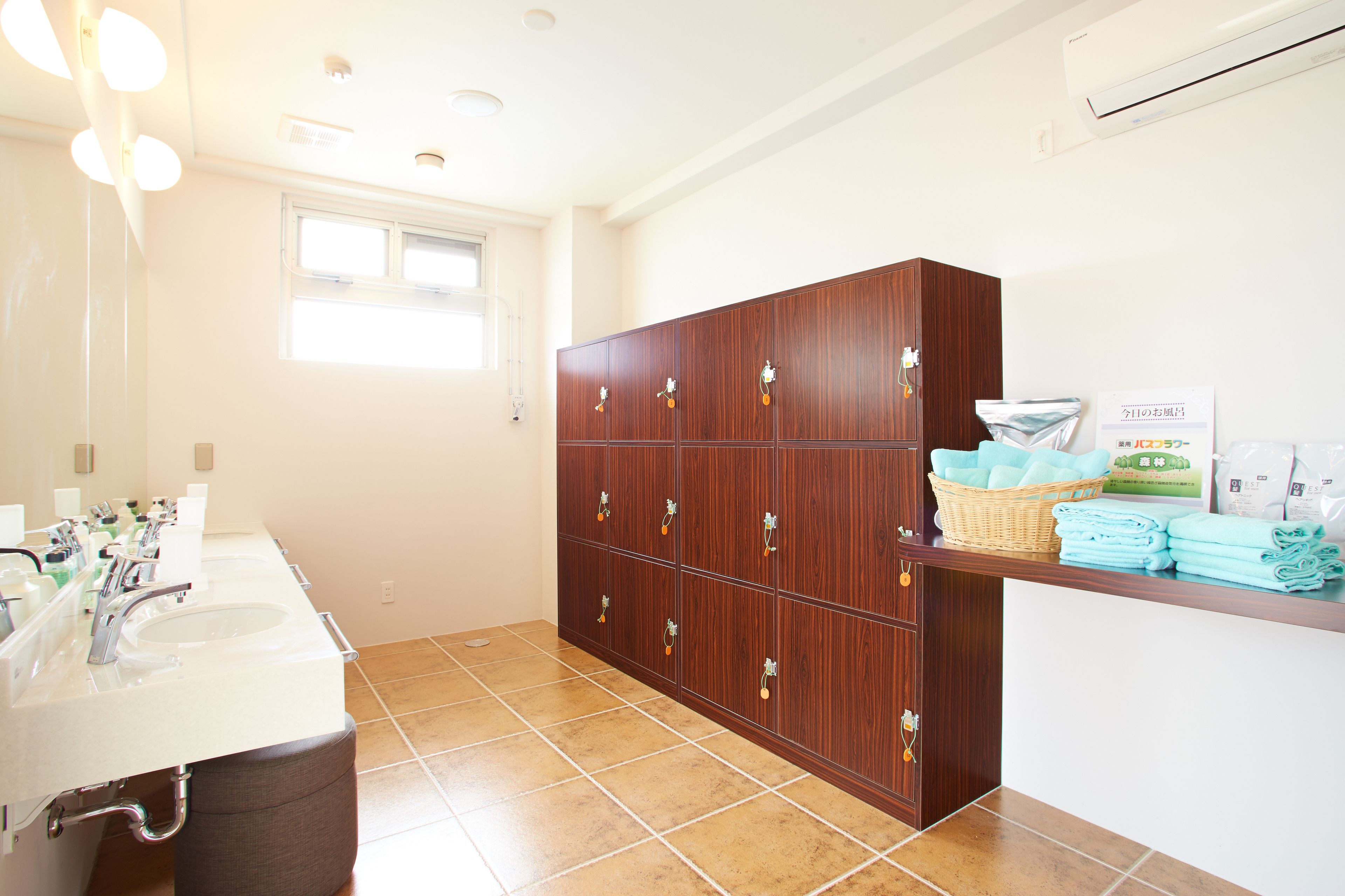 A hotel bathroom with multiple sinks, a wooden cabinet with hooks, and a counter with towels and toiletries.