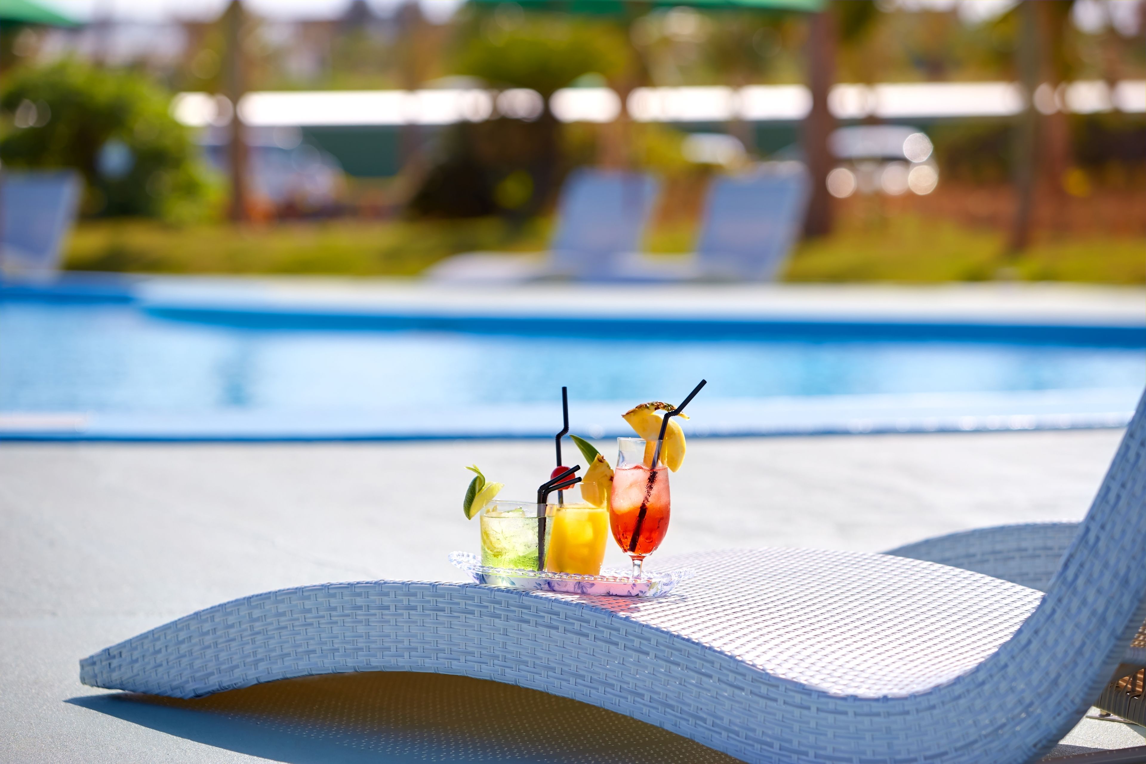 A poolside lounge chair with a tray of tropical drinks.