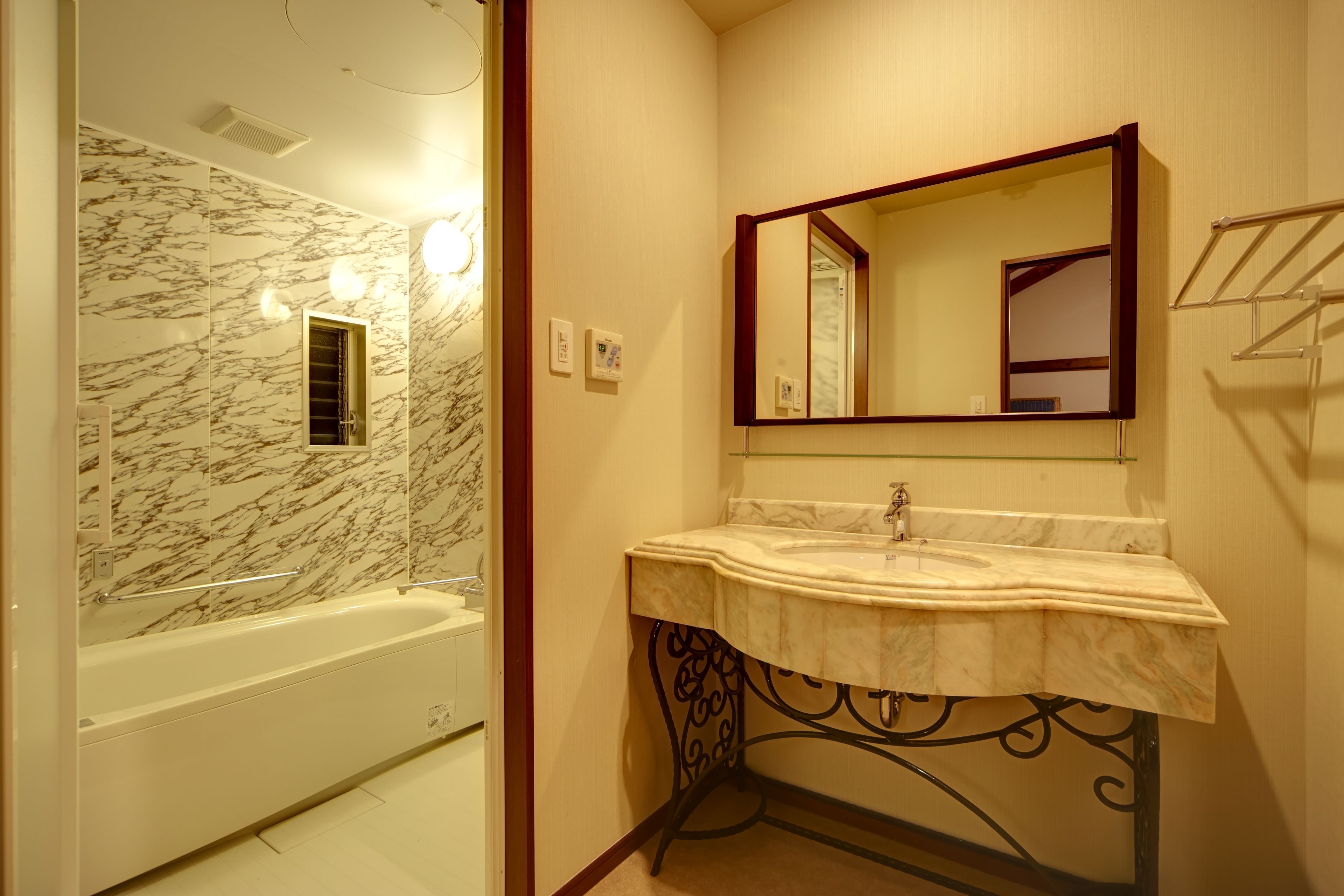 A bathroom with a marble wall, a bathtub, a sink with a marble countertop, and a mirror with a wooden frame.