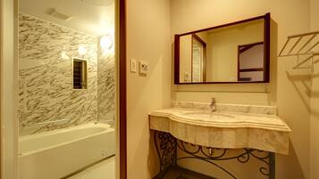 A bathroom with a marble wall, a bathtub, a sink with a marble countertop, and a mirror with a wooden frame.