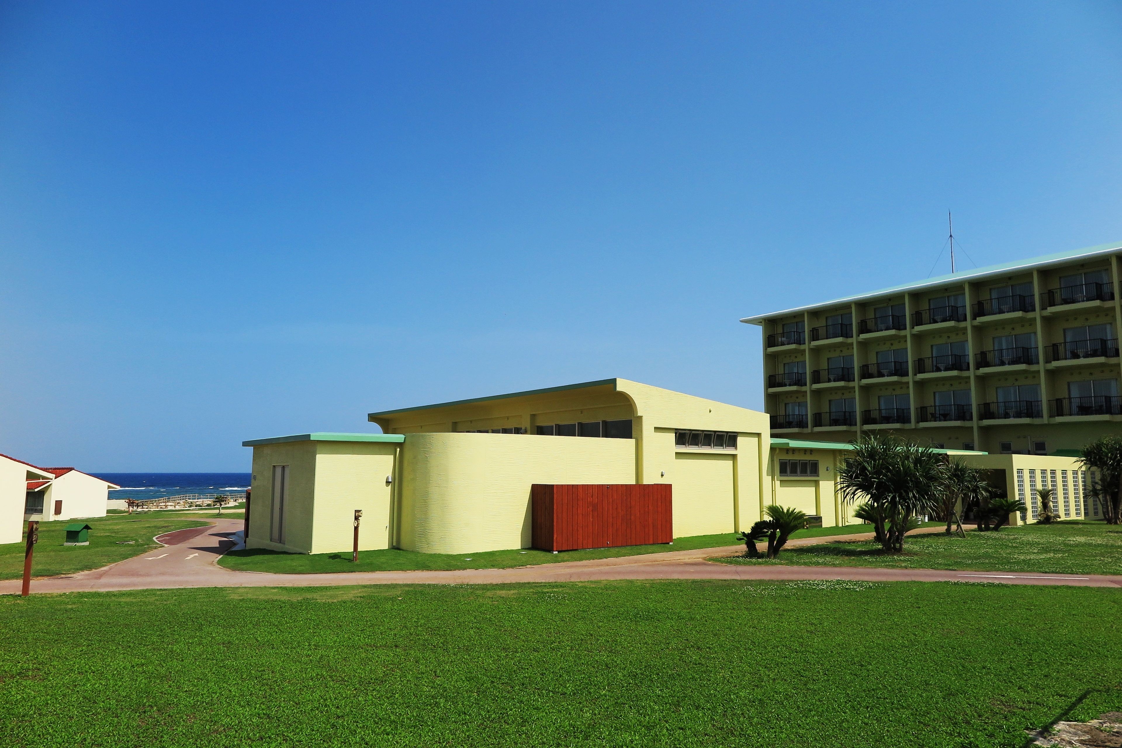 A building with a flat roof and a large window, surrounded by a well-maintained lawn and a clear sky.