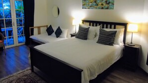 Una cama doble con cabecera de madera, dos mesitas de noche con lámparas, un cuadro abstracto grande en la pared y un ventanal corredero que da a un espacio exterior.