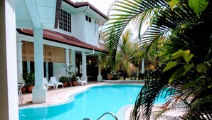 Una piscina con un borde de baldosas, sillas reclinables blancas y plantas en macetas.