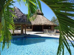 Una piscina con sillas de descanso y una estructura de techo de paja.
