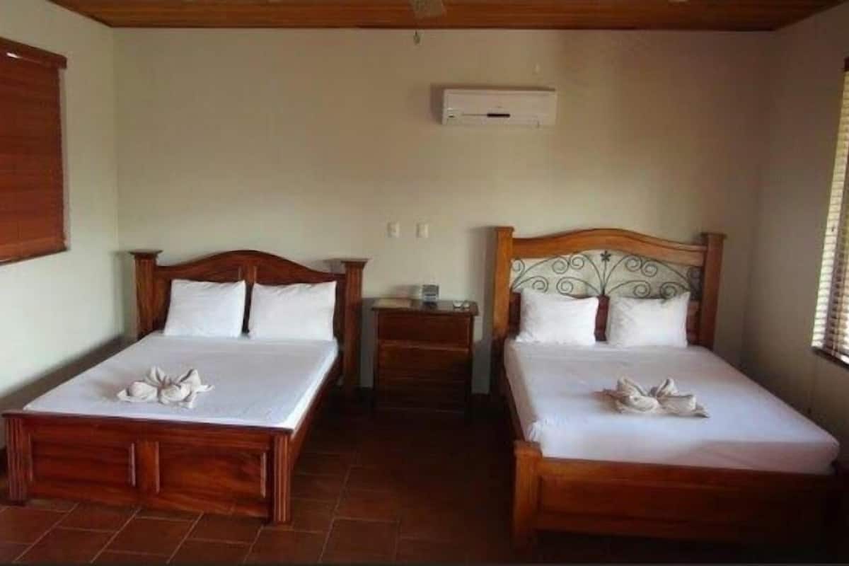 A hotel room with two wooden beds, a small bedside table, and a wall-mounted air conditioning unit.