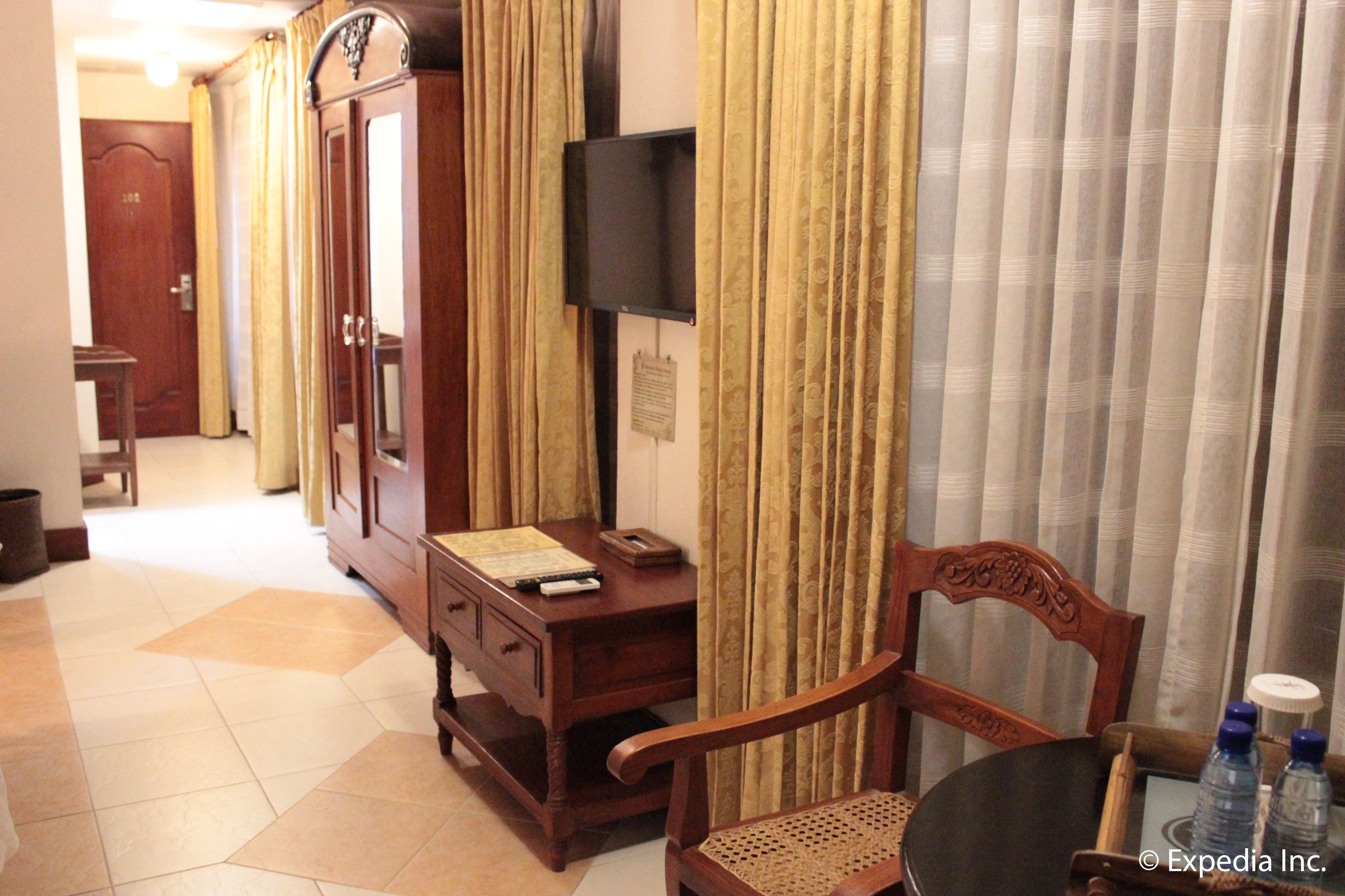 Habitación de hotel con un escritorio de madera, una silla, un televisor montado en la pared y una cama con cortinas.