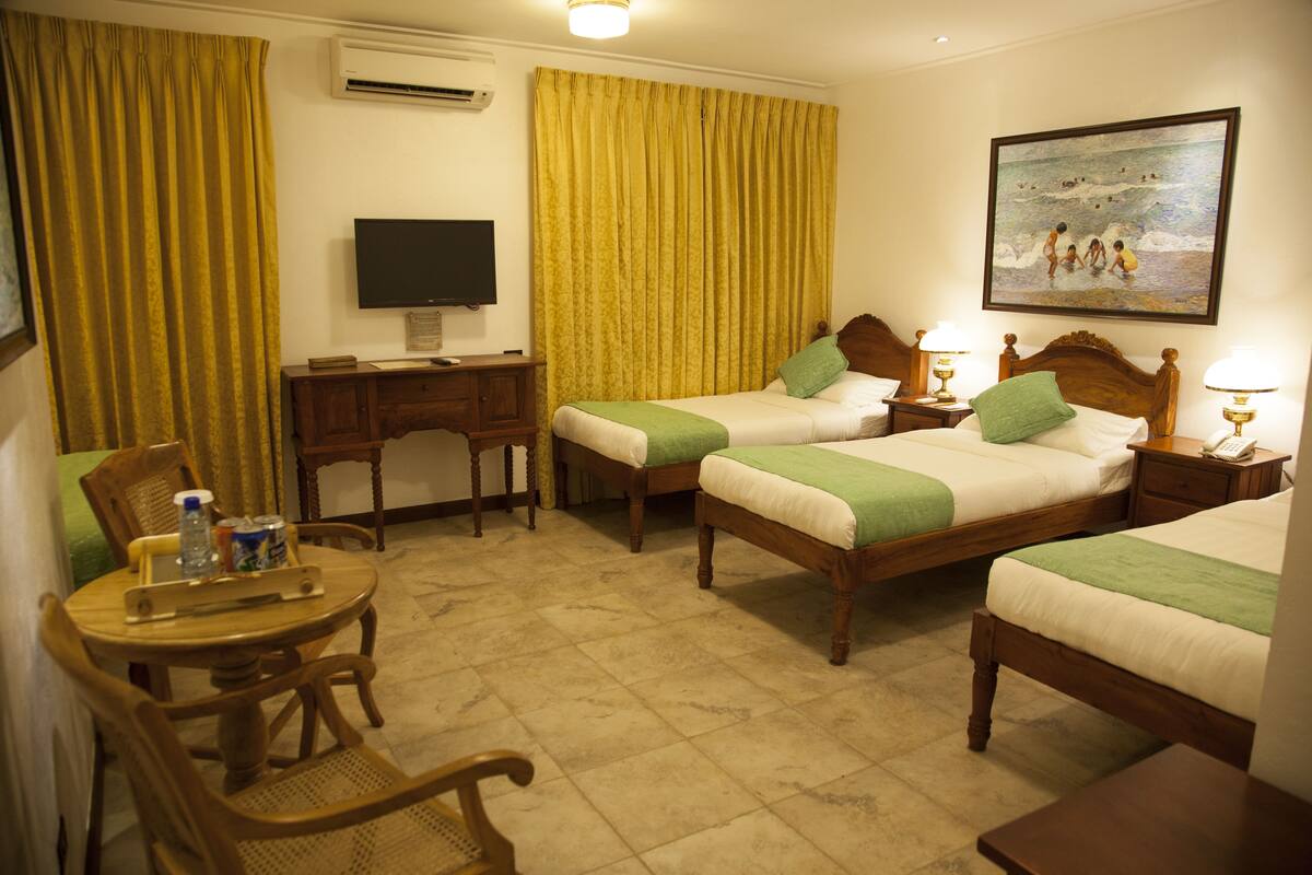 A hotel room with two beds, a desk, a television, and a painting on the wall.